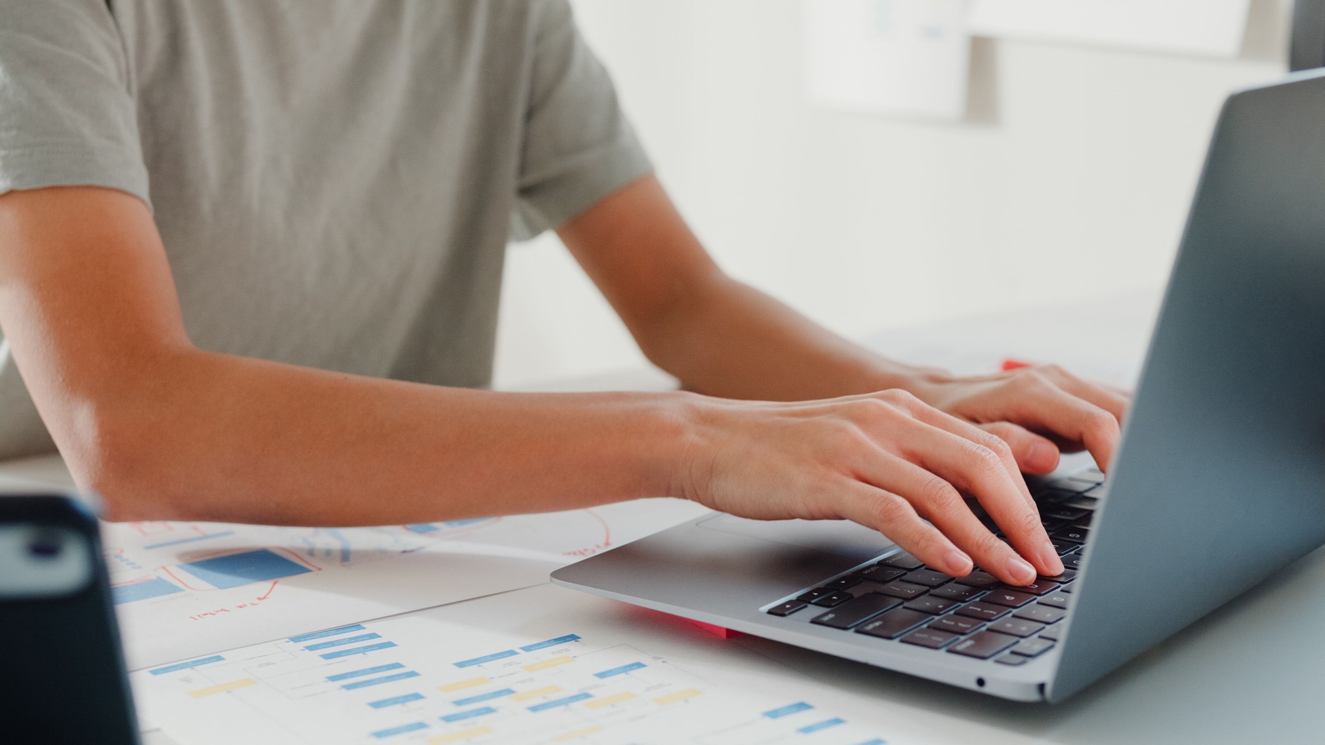 Close-up Young girl IT development programmer typing on keyboard coding programming fixing data code on laptop computer screen follow code plan in tablet and paperwork on table at house office.